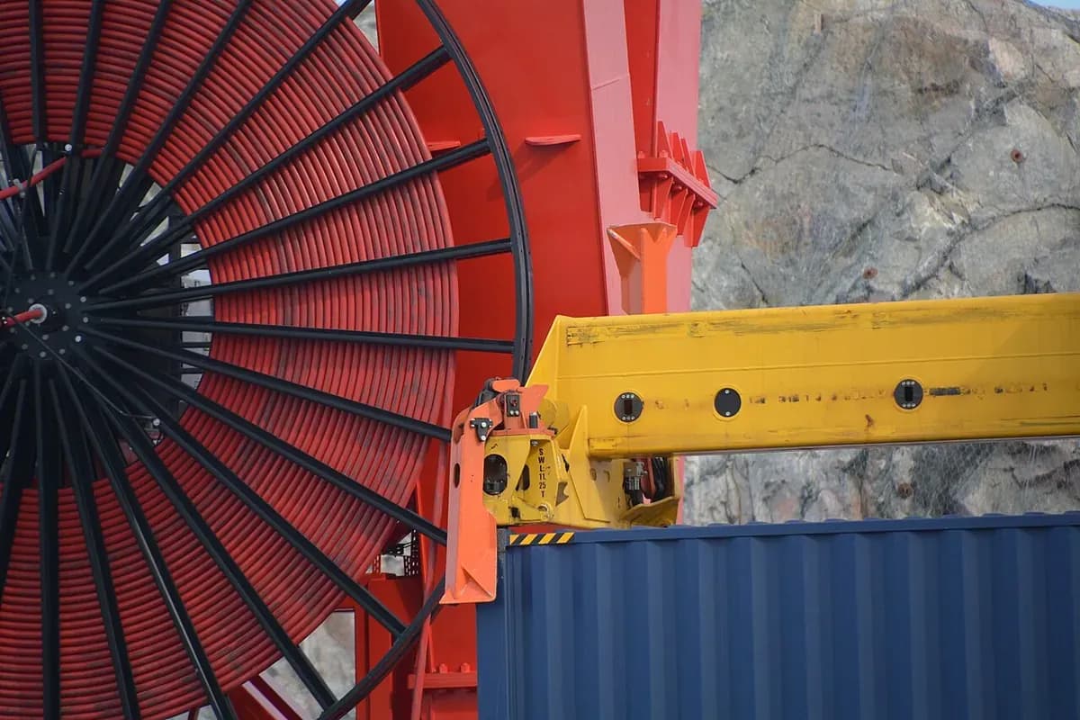 A spoked cable reel wound with red cable beside the yellow spreader of a container-handling crane