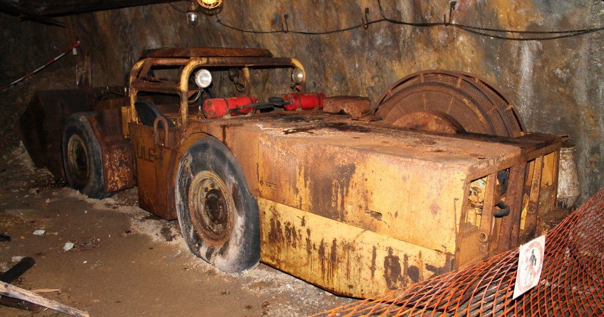 A historic electric load-haul-dump loader with a cable reel at its rear, parked in an underground drift with cables hung along the wall
