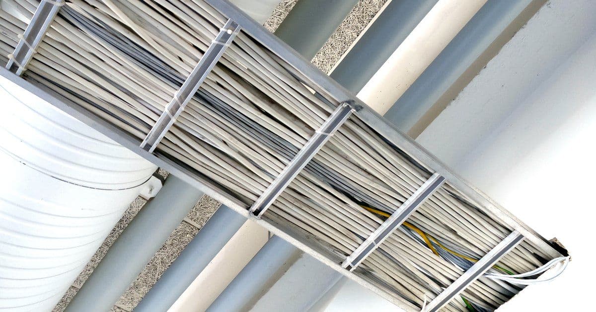 A cable tray packed with grey cables, fixed under a ceiling beside large ventilation ducts