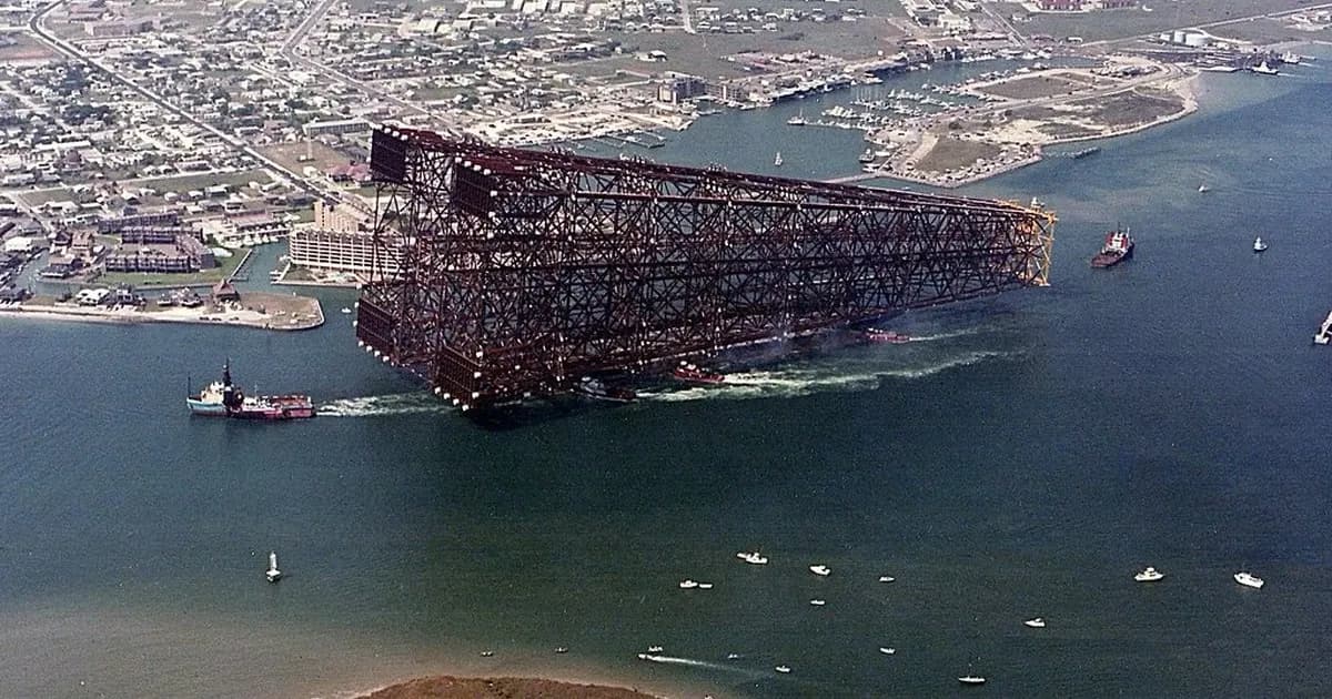 Offshore platform structure being towed by tugboats past a harbour