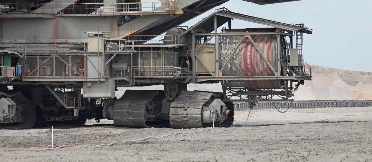A large cable reel on the crawler frame of a bucket-wheel spreader in an open-cut mine, with a red power cable wound on the drum and paid out across the ground