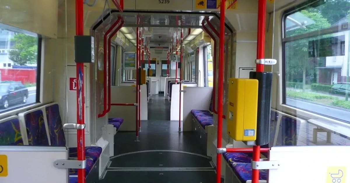 Interior of an empty rail passenger vehicle with red handrails and fixed seating