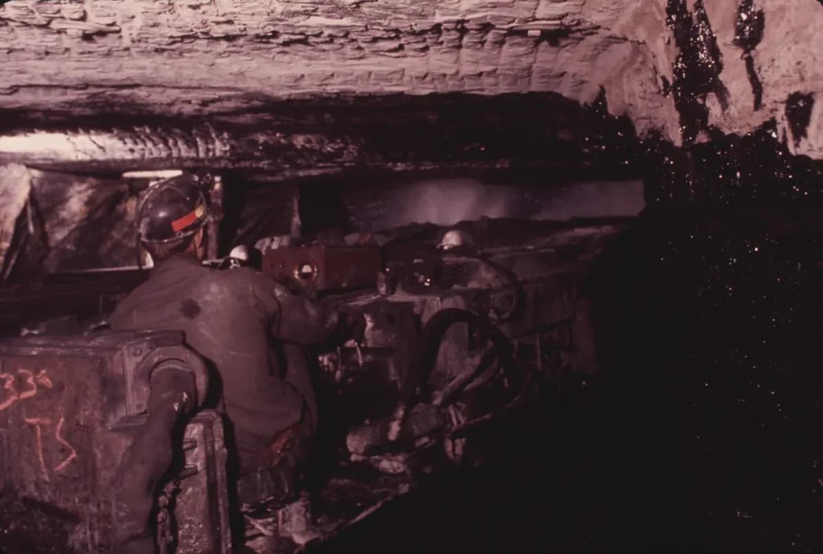 A miner at the controls of a continuous mining machine with water sprays at the coal face