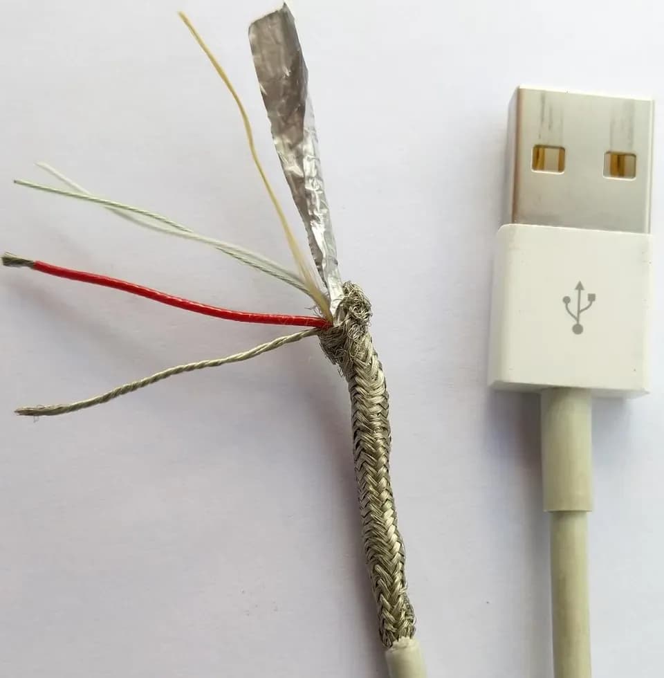A cut-open cable showing a metal braid, a foil wrap, a bare wire and coloured insulated wires next to its plug