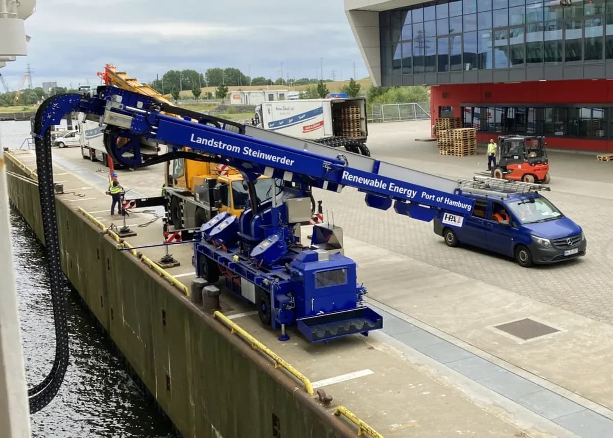 A blue mobile crane on a quay feeding a power cable in a cable chain over the edge to a ship