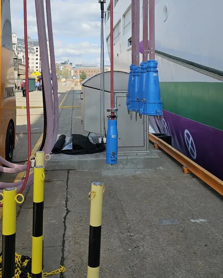 Blue high-voltage shore connection plugs hanging on cables beside a docked passenger ship