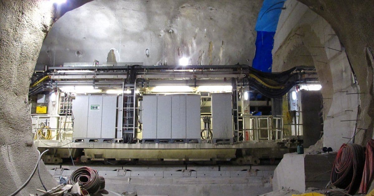 A tunnel boring machine back-up with grey electrical cabinets and cable trays inside a metro station tunnel under construction