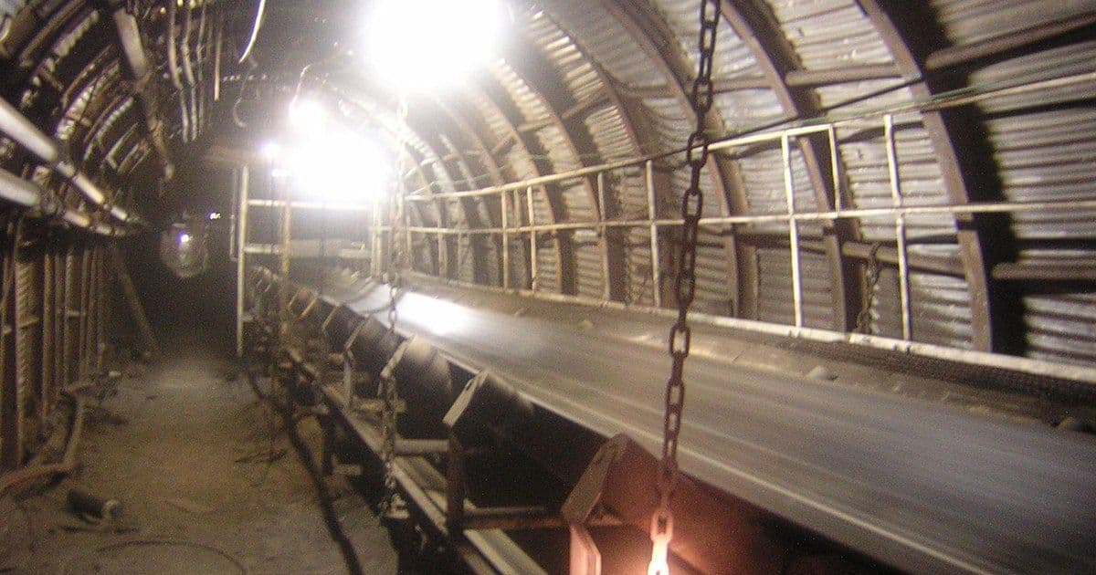 An underground belt conveyor in an arched coal mine roadway, with pipes and cables along the side
