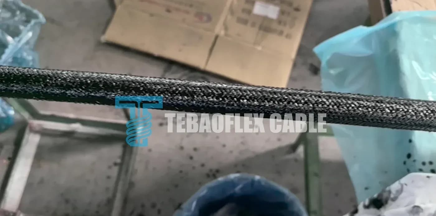 Close-up of a finished cable showing a dense, coarse, dark textile braid with a regular lay over a black inner layer.