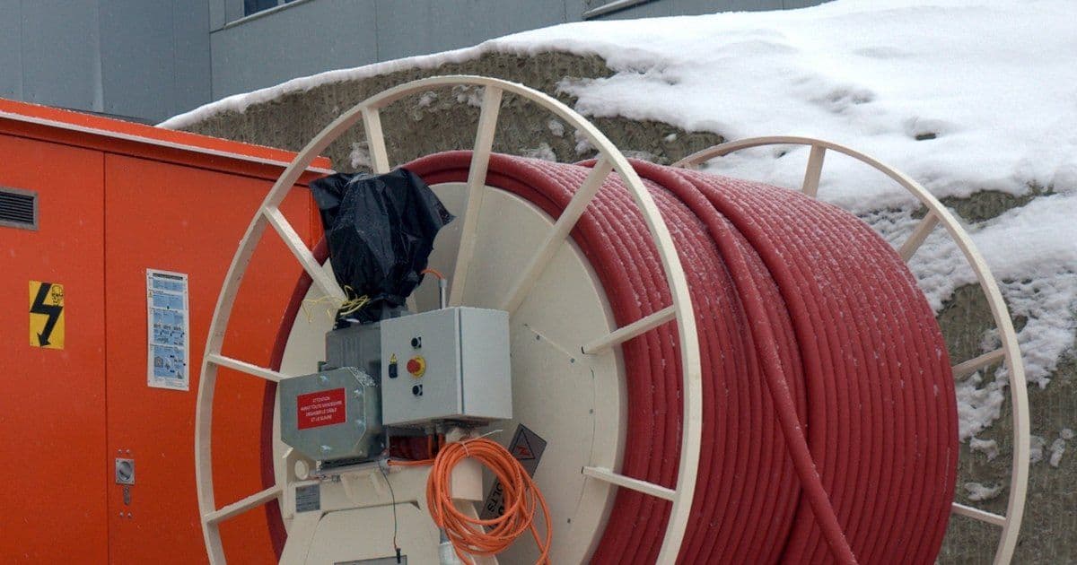 A cable drum wound with red cable beside an orange provisional medium-to-low-voltage substation on a snowy site