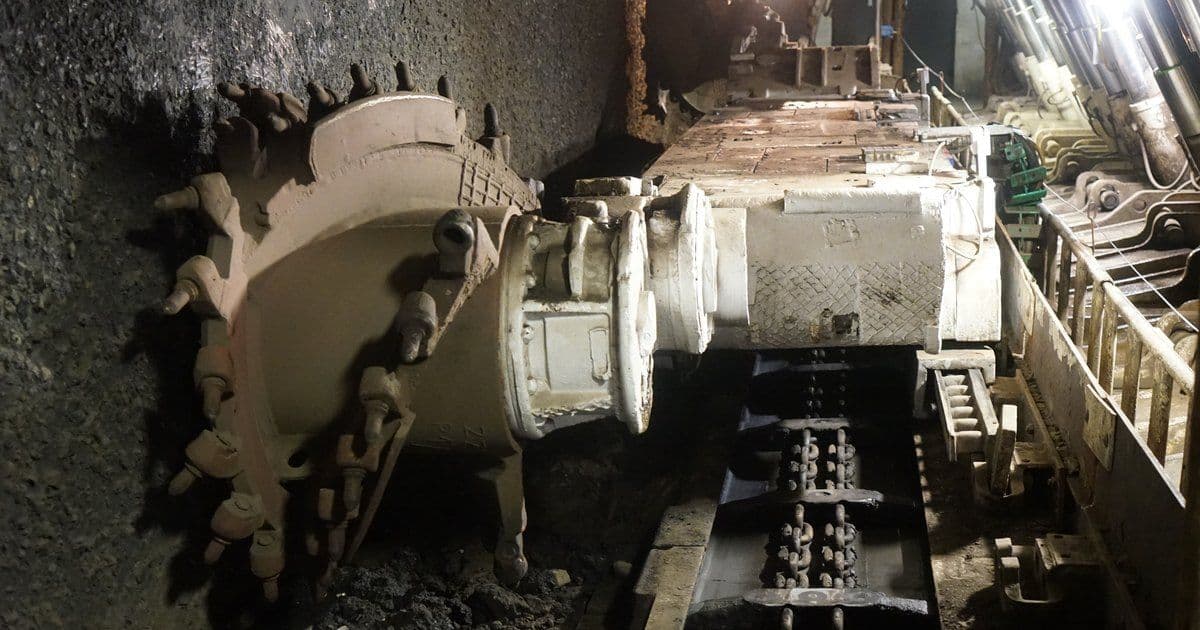A longwall shearer's cutting drum beside an armoured face conveyor and roof supports in a historic underground coal mine