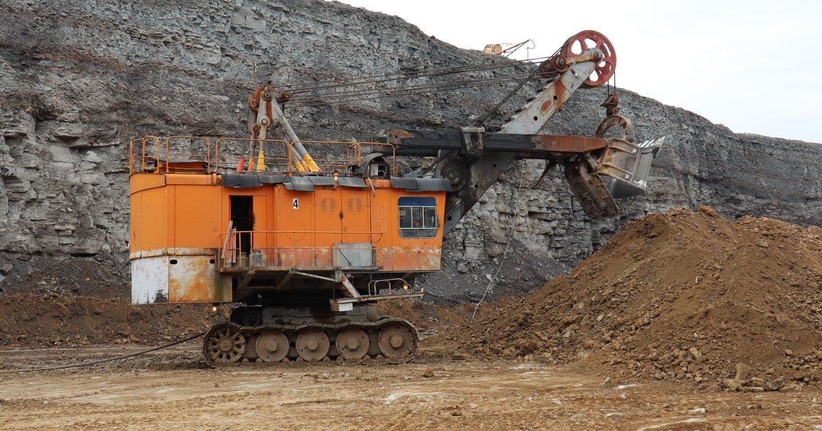 An orange rope shovel at an open-pit mine with its trailing cable lying on the pit floor